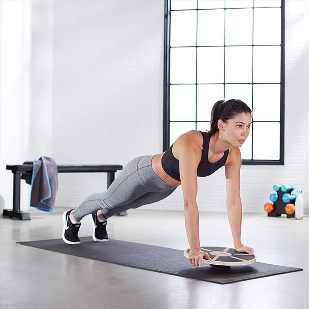 A woman using AlephNeta CoreBalance for push-ups on a yoga mat in a bright gym setting.